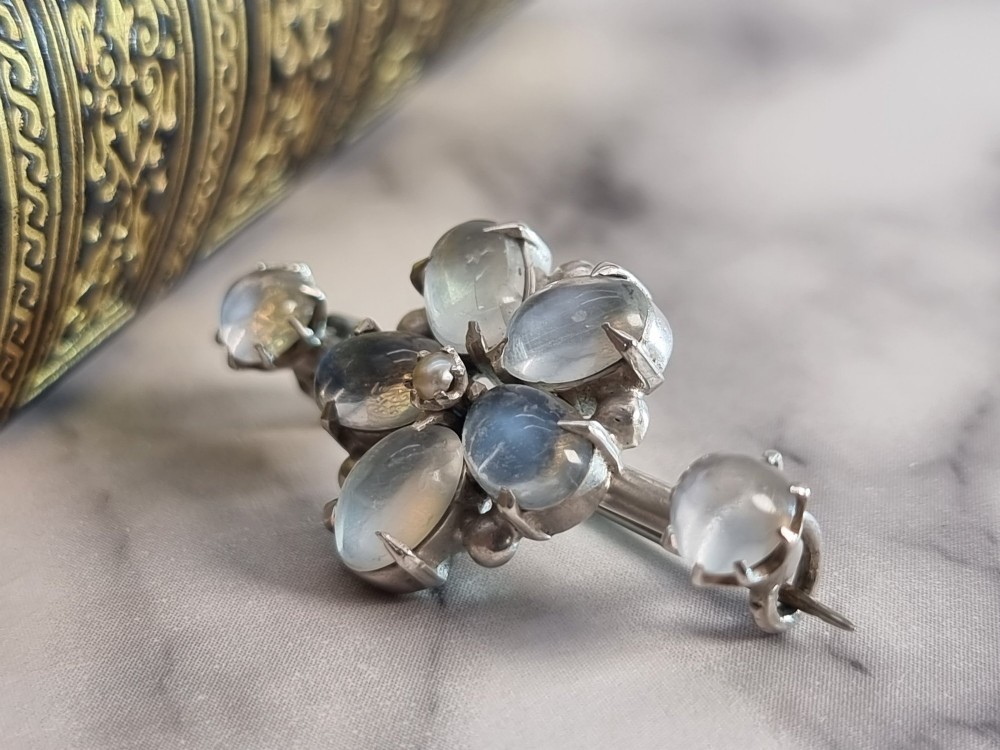An antique silver bar brooch featuring a central flower cluster of oval cabochon moonstones flanked by single moonstones on either side. View V