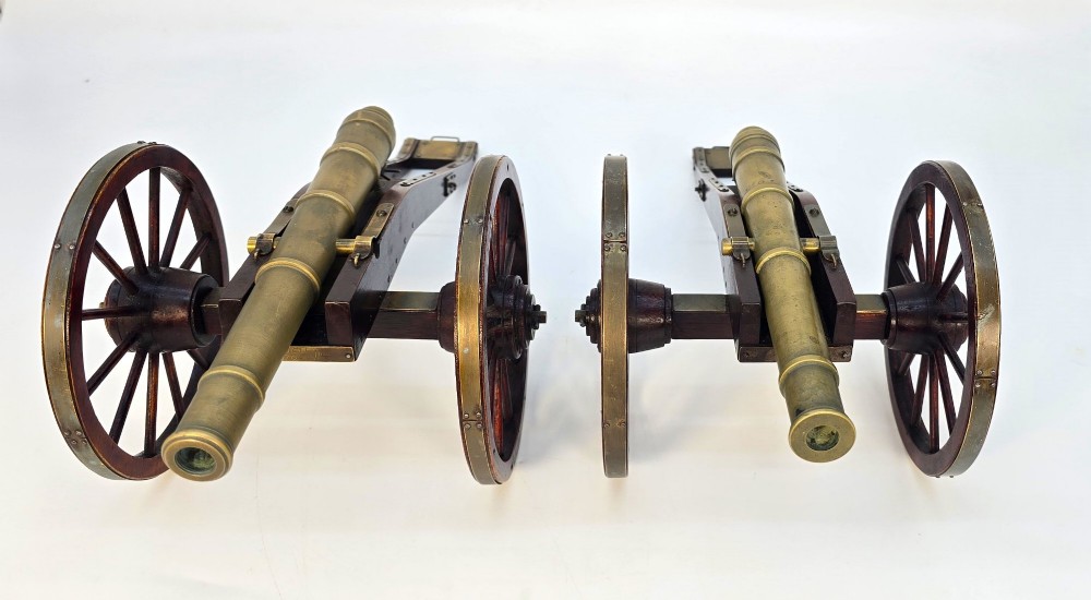 A pair of 1920s model field cannons featuring cast brass barrels mounted on dark wooden spoked-wheel carriages. View II