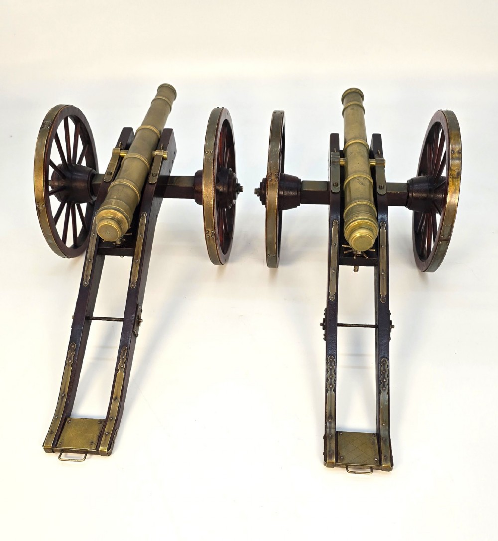 A pair of 1920s model field cannons featuring cast brass barrels mounted on dark wooden spoked-wheel carriages. View IV