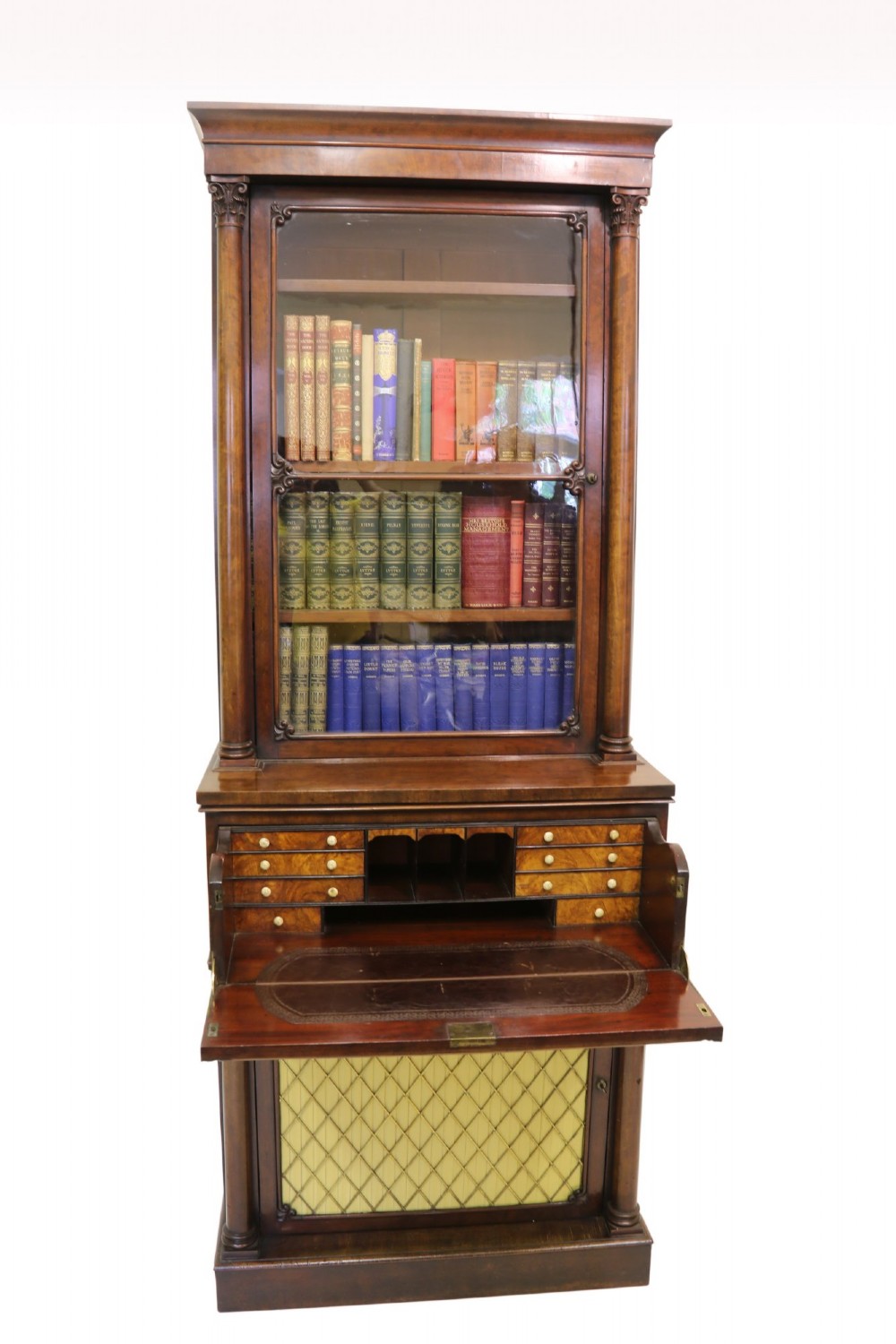 A Regency mahogany secretaire bookcase featuring a glazed upper display cabinet, a drop-front writing drawer with a fitted interior, and reeded side columns.