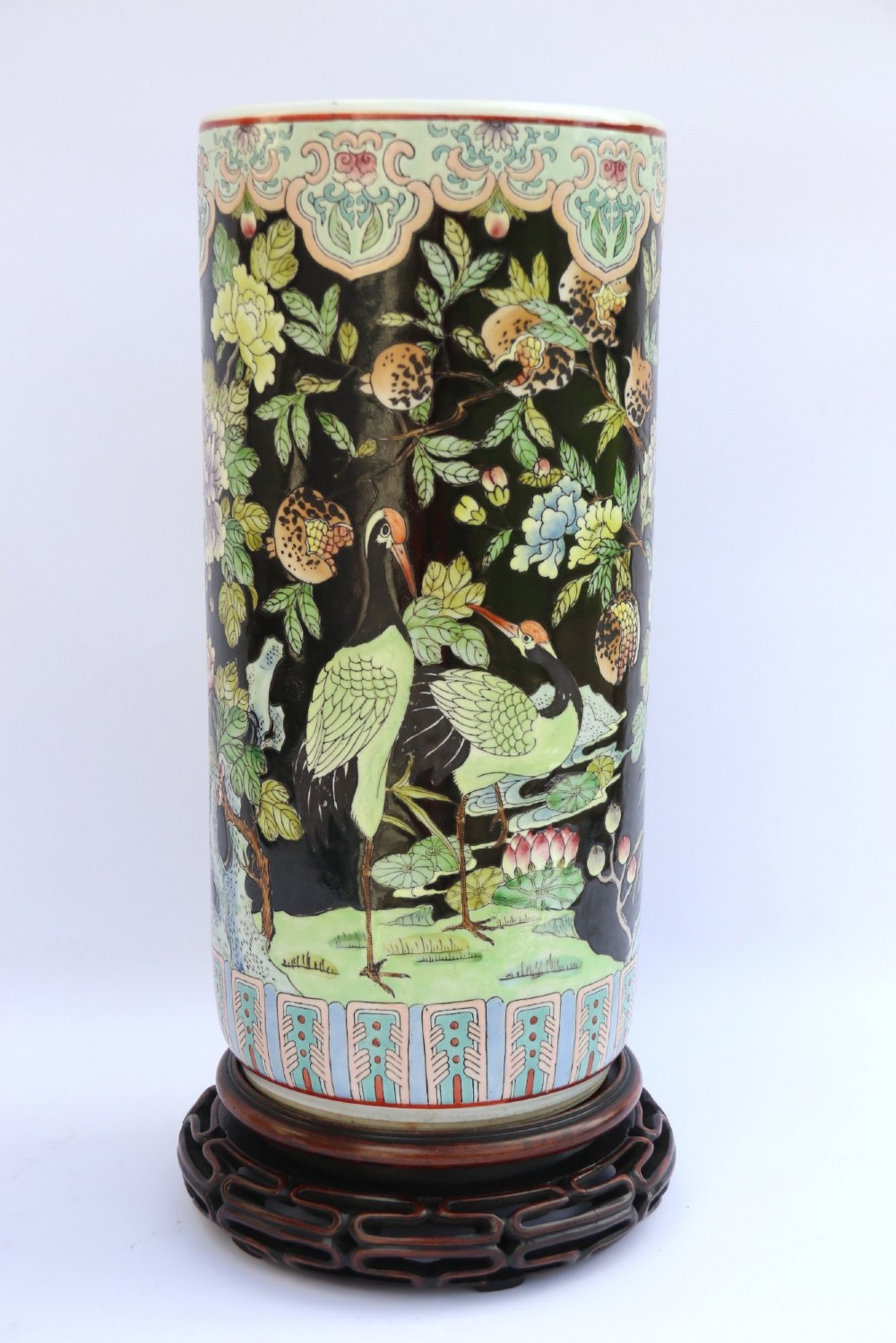 A cylindrical Chinese famille noire porcelain vase decorated with colourful birds and peony flowers set against a black ground, resting on a carved dark hardwood stand. View III