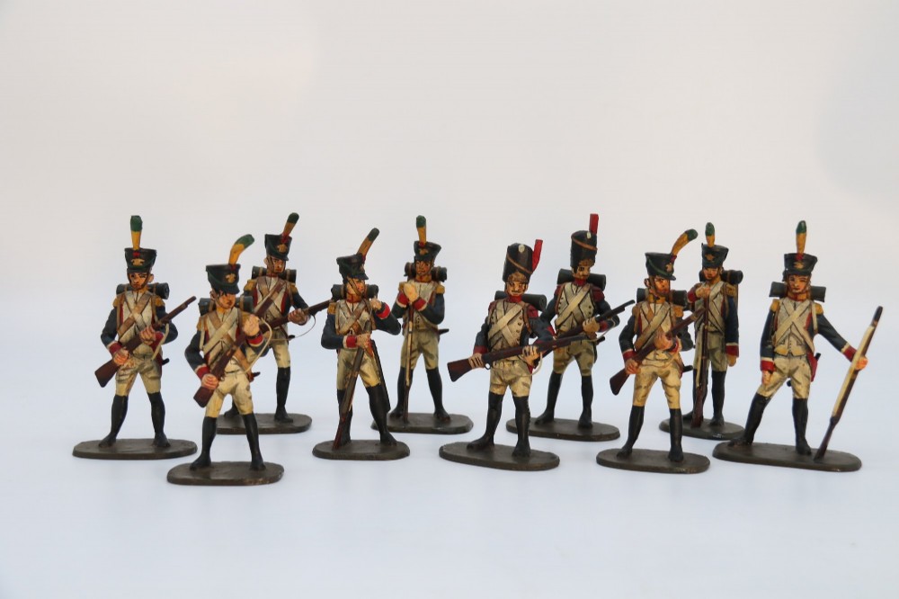 A group of ten hand-carved and painted wooden figures depicting Napoleonic infantry soldiers with muskets standing on individual oval bases. View X