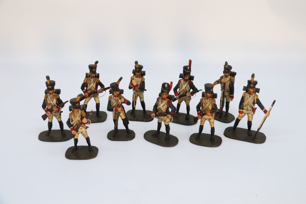 A group of ten hand-carved and painted wooden figures depicting Napoleonic infantry soldiers with muskets standing on individual oval bases. View XI
