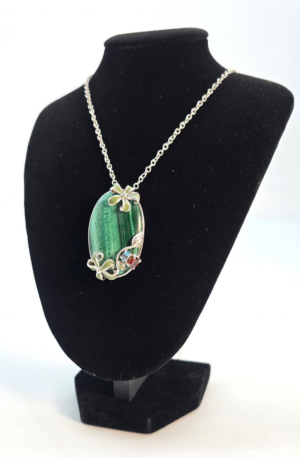 An oval green banded malachite pendant set in silver with floral enamel embellishments and small accent stones on a fine chain.