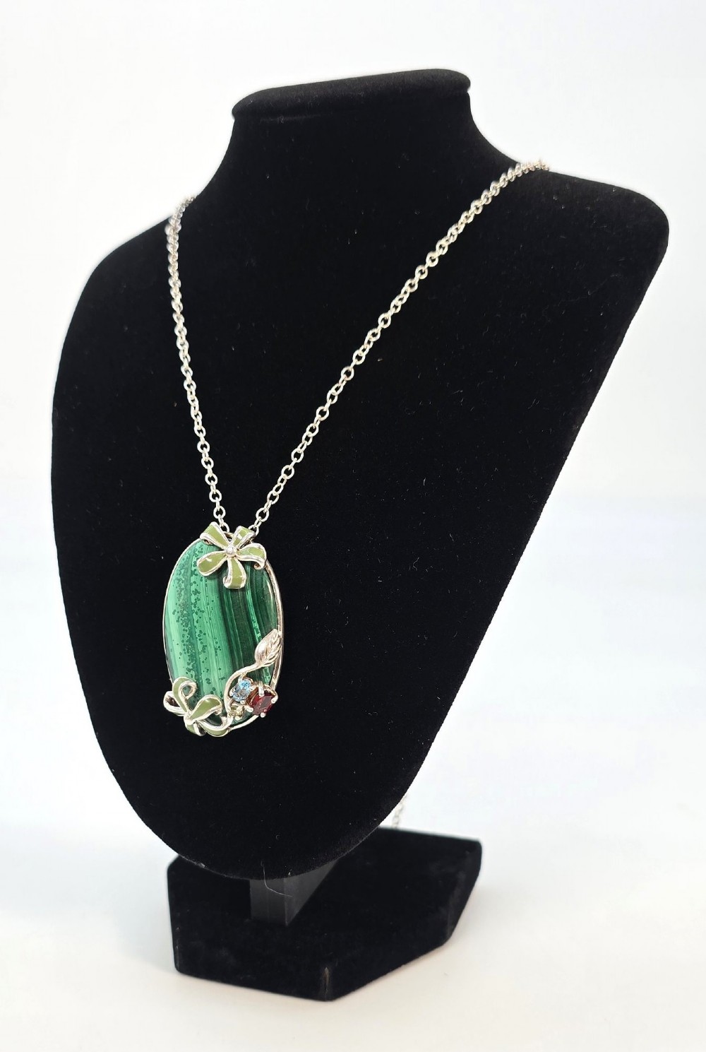 An oval green banded malachite pendant set in silver with floral enamel embellishments and small accent stones on a fine chain. View II