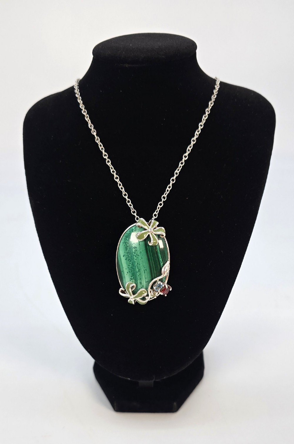 An oval green banded malachite pendant set in silver with floral enamel embellishments and small accent stones on a fine chain. View VII