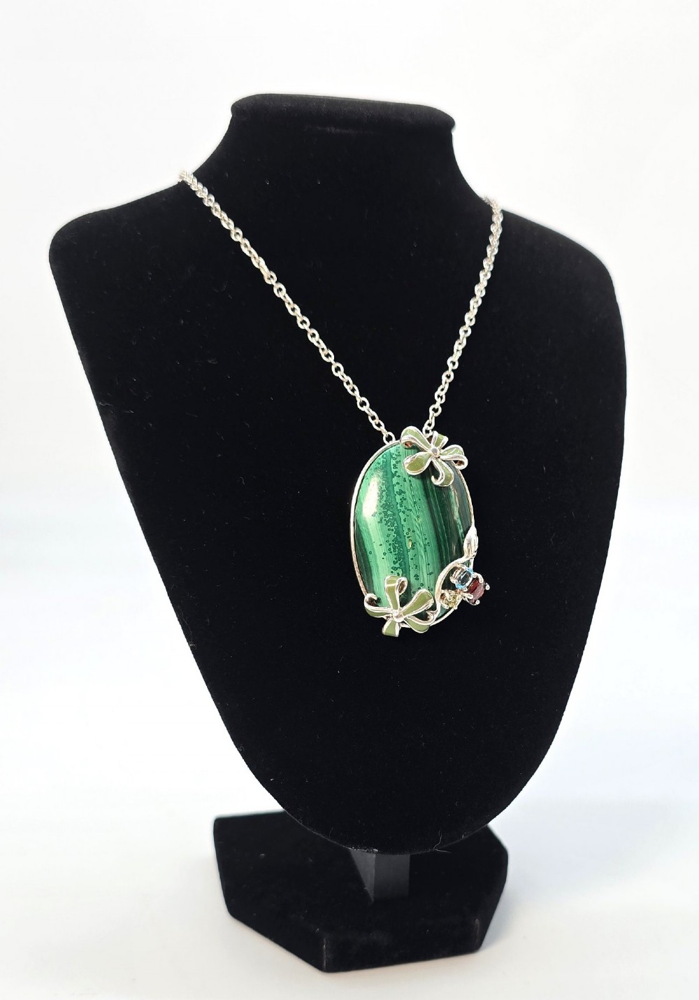 An oval green banded malachite pendant set in silver with floral enamel embellishments and small accent stones on a fine chain. View VIII