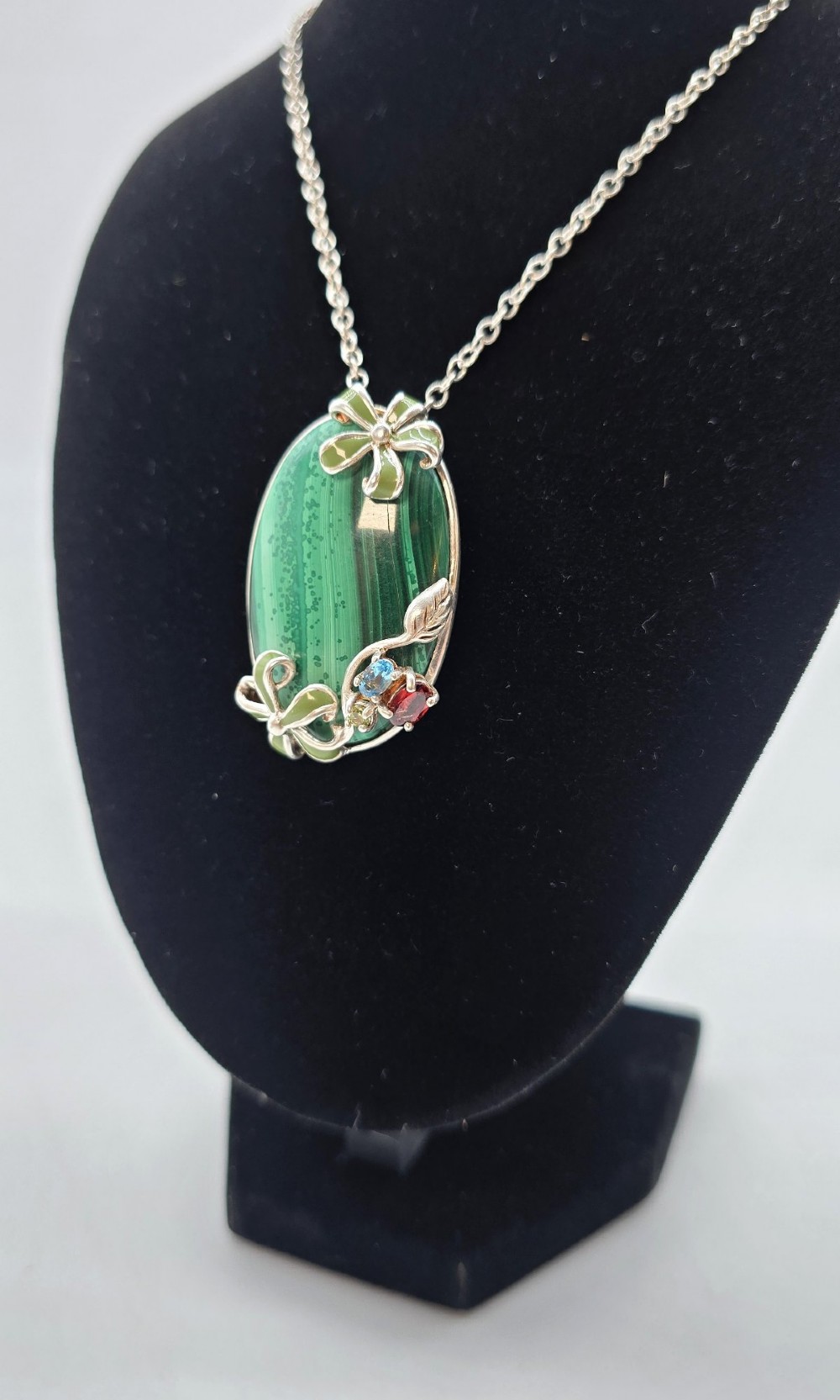 An oval green banded malachite pendant set in silver with floral enamel embellishments and small accent stones on a fine chain. View IX