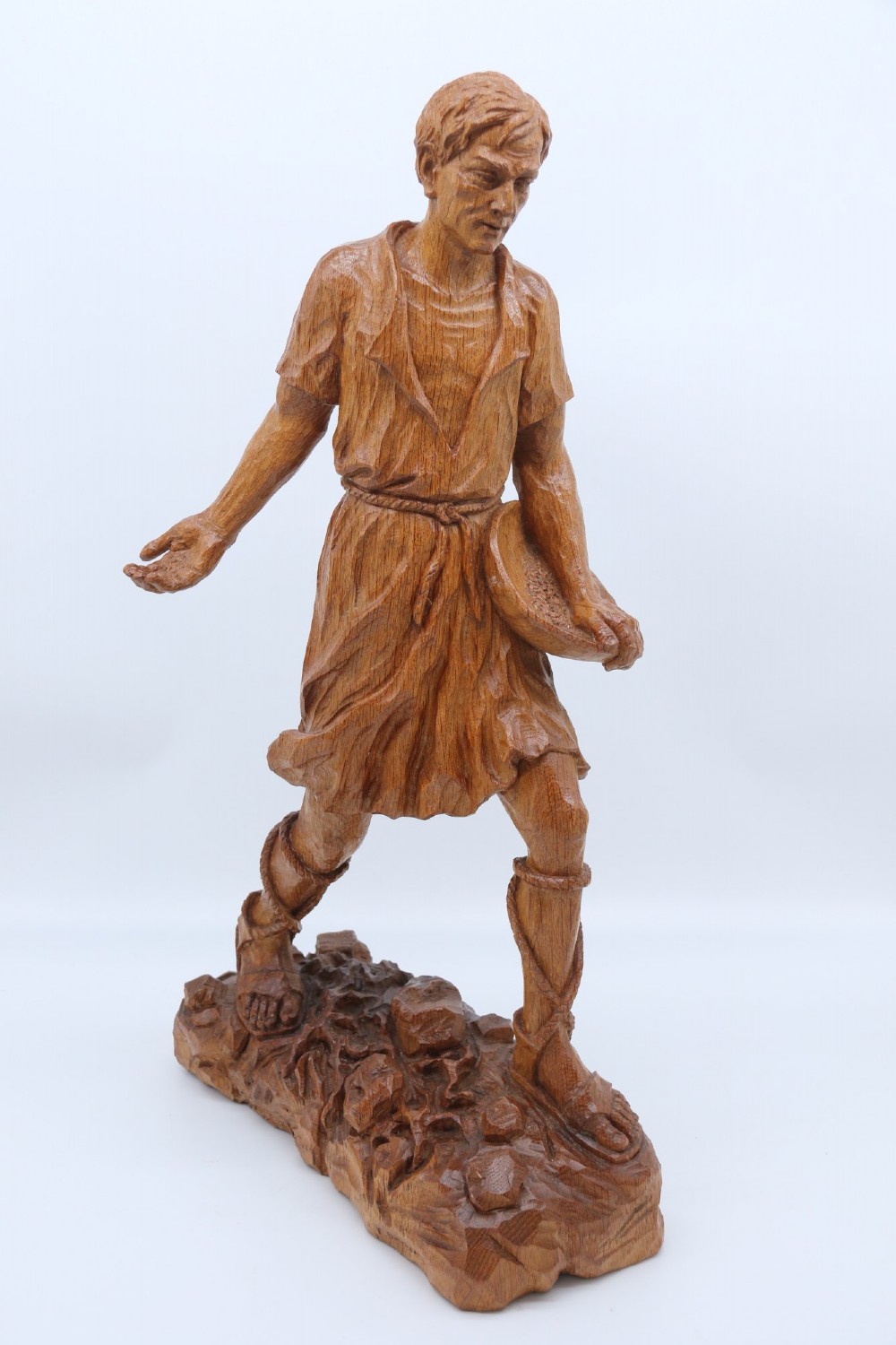 A hand-carved golden oak wooden sculpture of a male farm worker standing on a carved naturalistic base while holding a shallow tray.