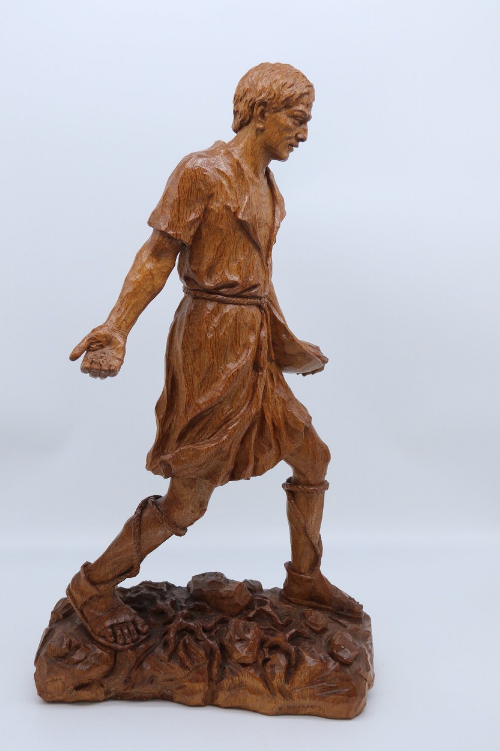 A hand-carved golden oak wooden sculpture of a male farm worker standing on a carved naturalistic base while holding a shallow tray. View III
