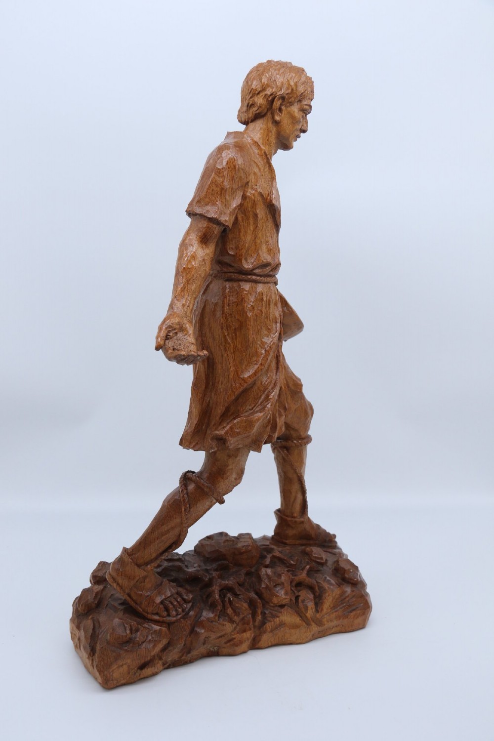 A hand-carved golden oak wooden sculpture of a male farm worker standing on a carved naturalistic base while holding a shallow tray. View IV