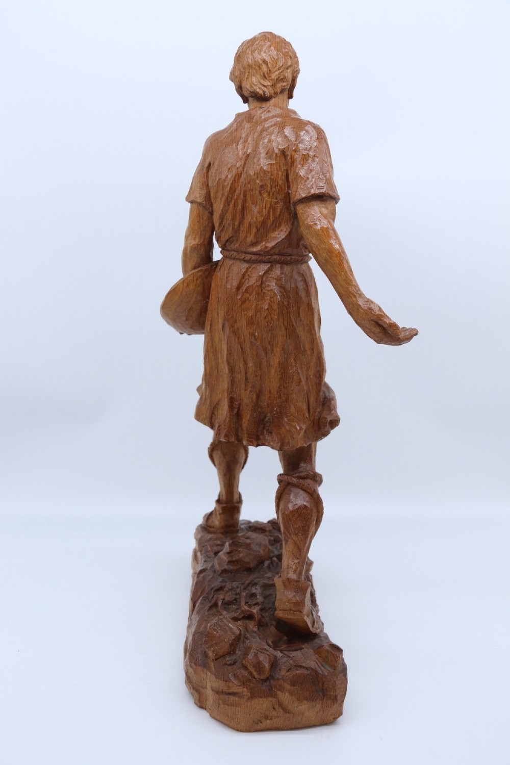 A hand-carved golden oak wooden sculpture of a male farm worker standing on a carved naturalistic base while holding a shallow tray. View V