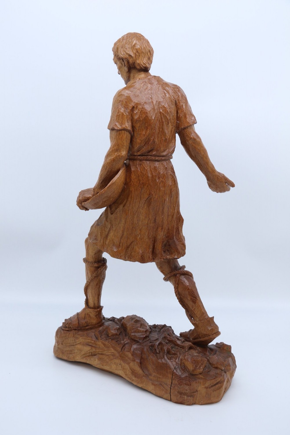 A hand-carved golden oak wooden sculpture of a male farm worker standing on a carved naturalistic base while holding a shallow tray. View VI