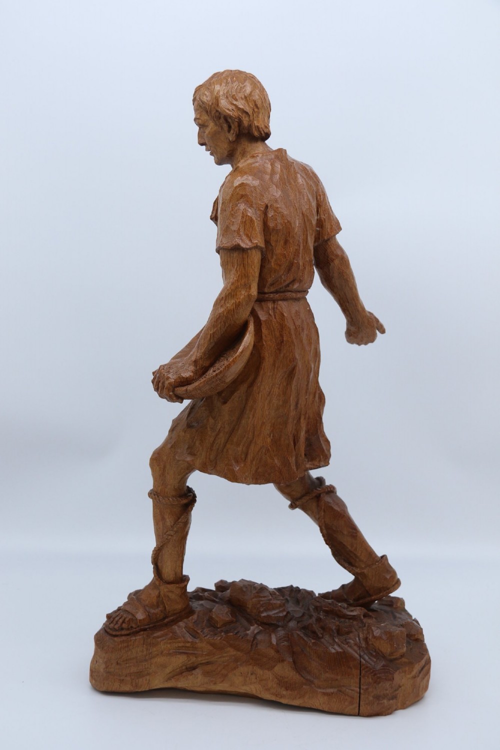 A hand-carved golden oak wooden sculpture of a male farm worker standing on a carved naturalistic base while holding a shallow tray. View VII