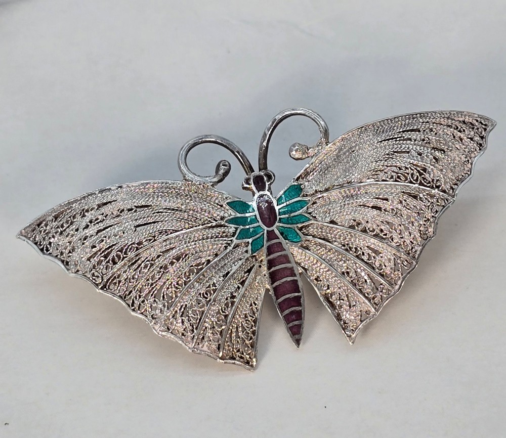 A silver filigree butterfly brooch featuring teal and purple enamelled body details. View II