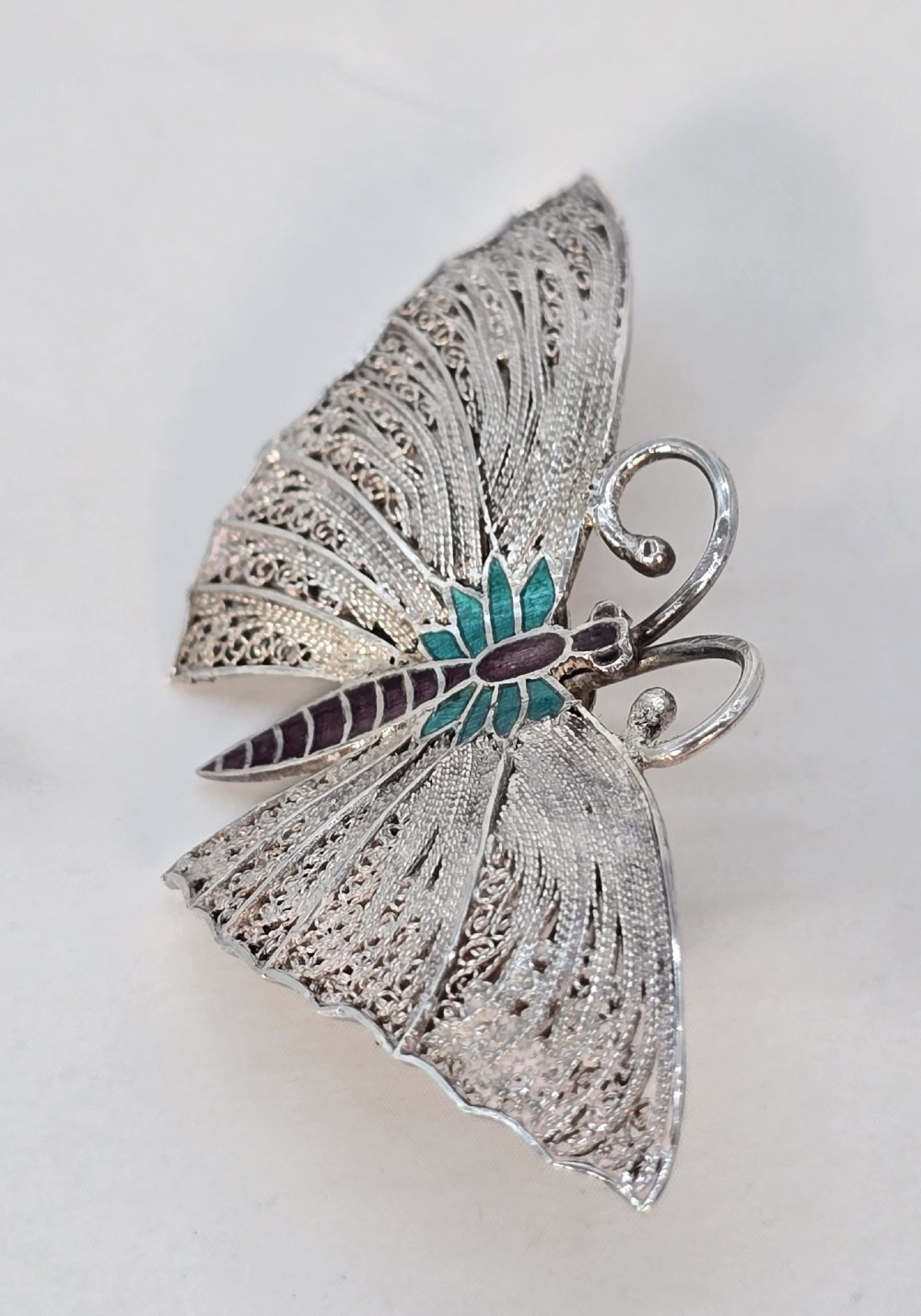 A silver filigree butterfly brooch featuring teal and purple enamelled body details. View IV