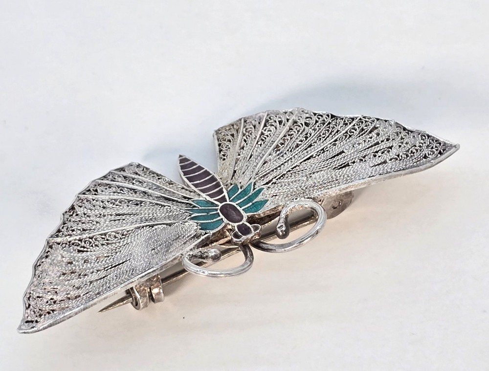 A silver filigree butterfly brooch featuring teal and purple enamelled body details. View V