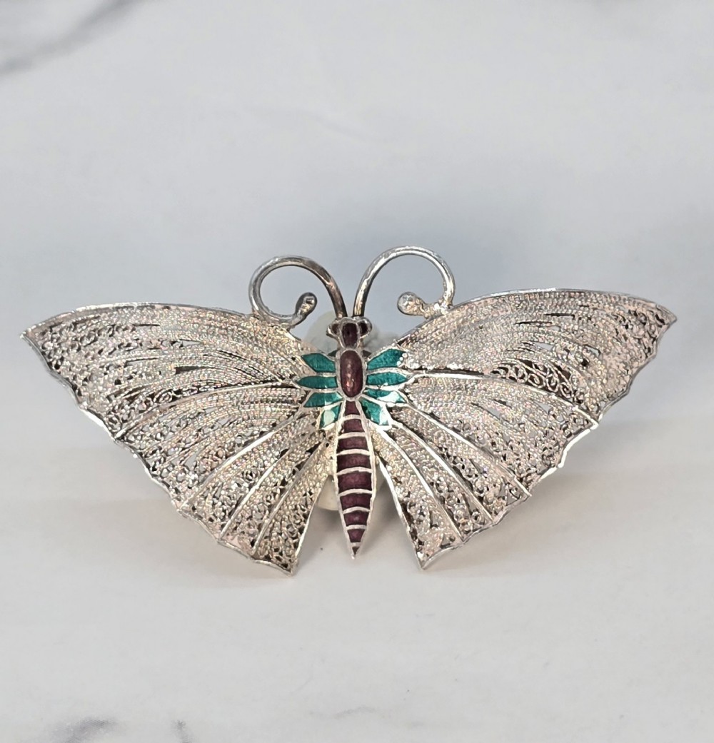 A silver filigree butterfly brooch featuring teal and purple enamelled body details. View VII