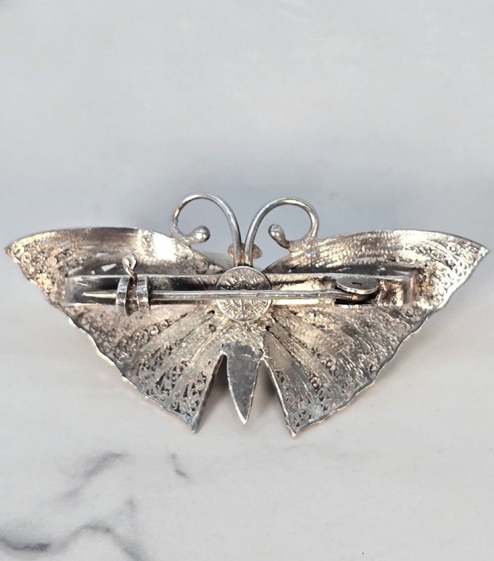 A silver filigree butterfly brooch featuring teal and purple enamelled body details. View VIII
