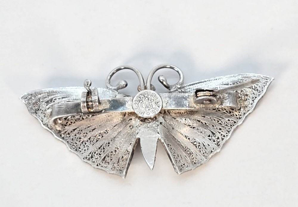 A silver filigree butterfly brooch featuring teal and purple enamelled body details. View IX