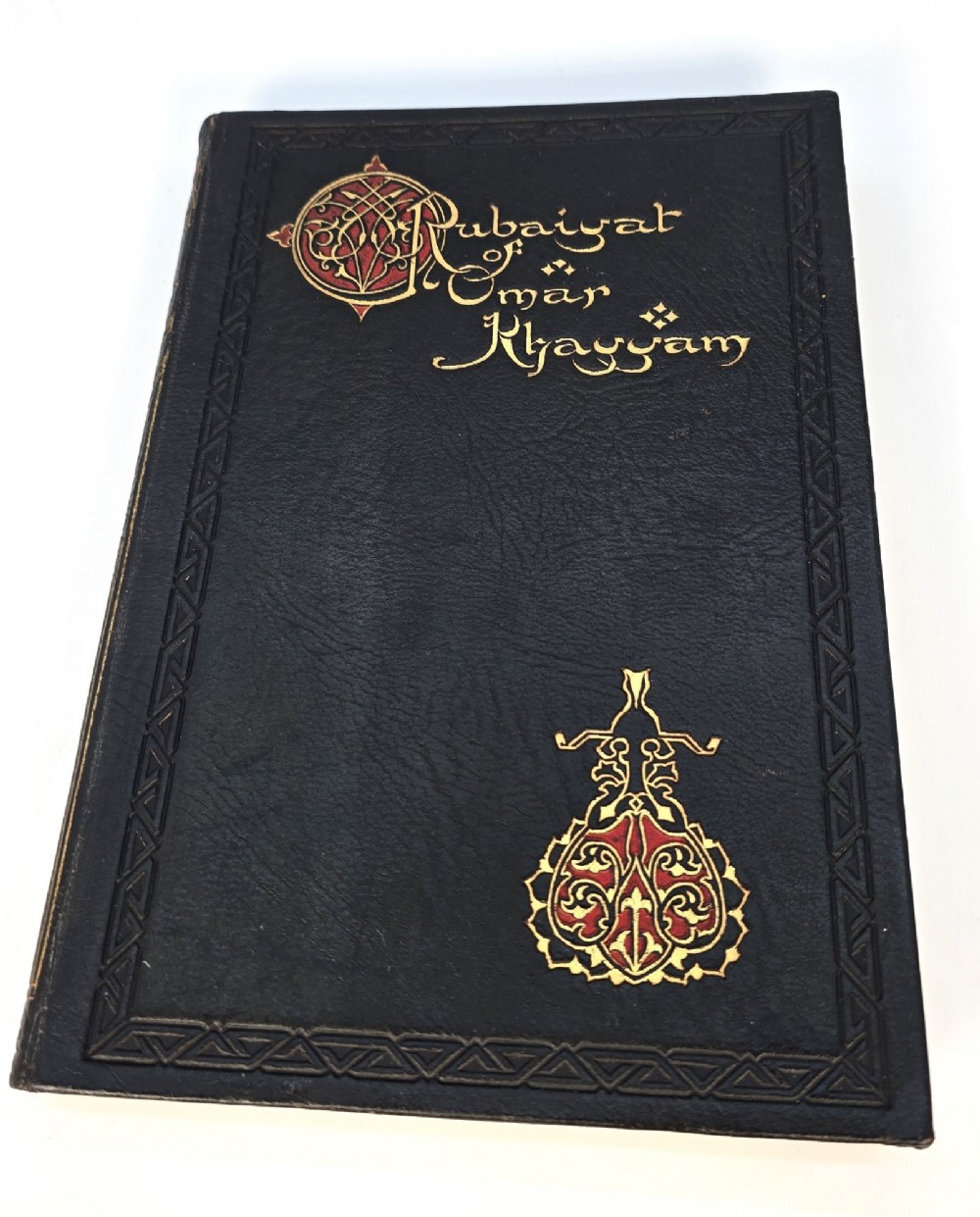 An Edwardian black leather bound edition of the Rubaiyat of Omar Khayyam featuring gilt and red embellished lettering with geometric corner tooling. View IV
