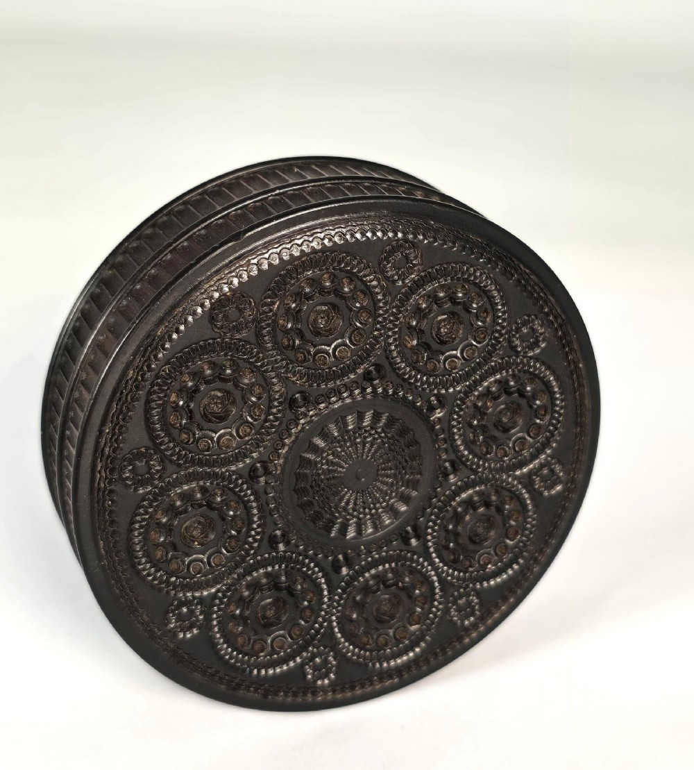 A circular black ebony snuff box with intricate engine-turned geometric patterns and raised beaded details on the lid. View II