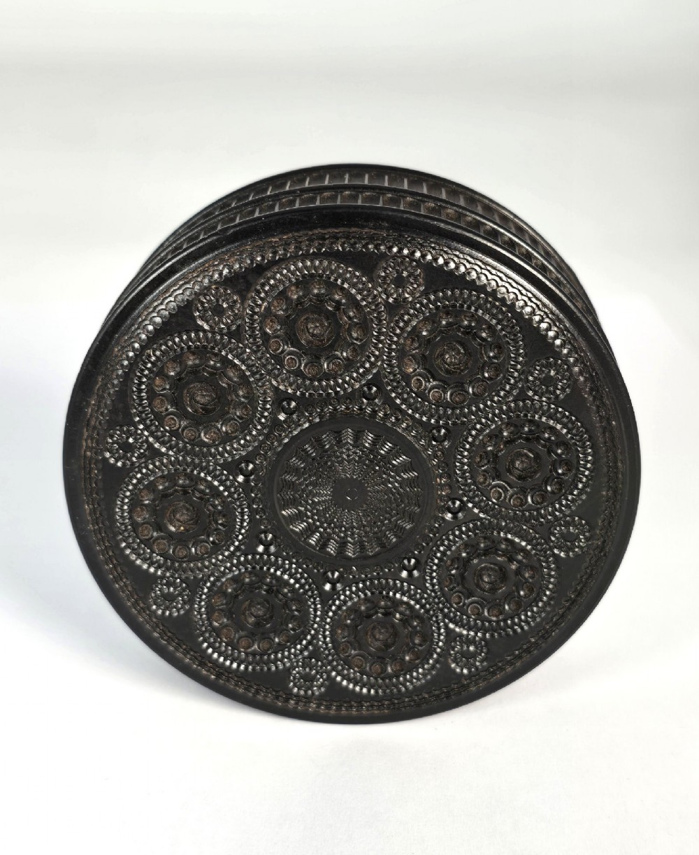 A circular black ebony snuff box with intricate engine-turned geometric patterns and raised beaded details on the lid. View III
