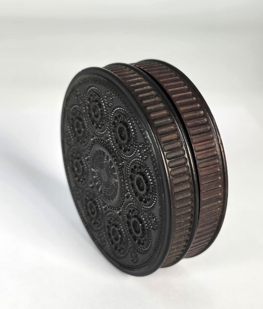 A circular black ebony snuff box with intricate engine-turned geometric patterns and raised beaded details on the lid. View IV