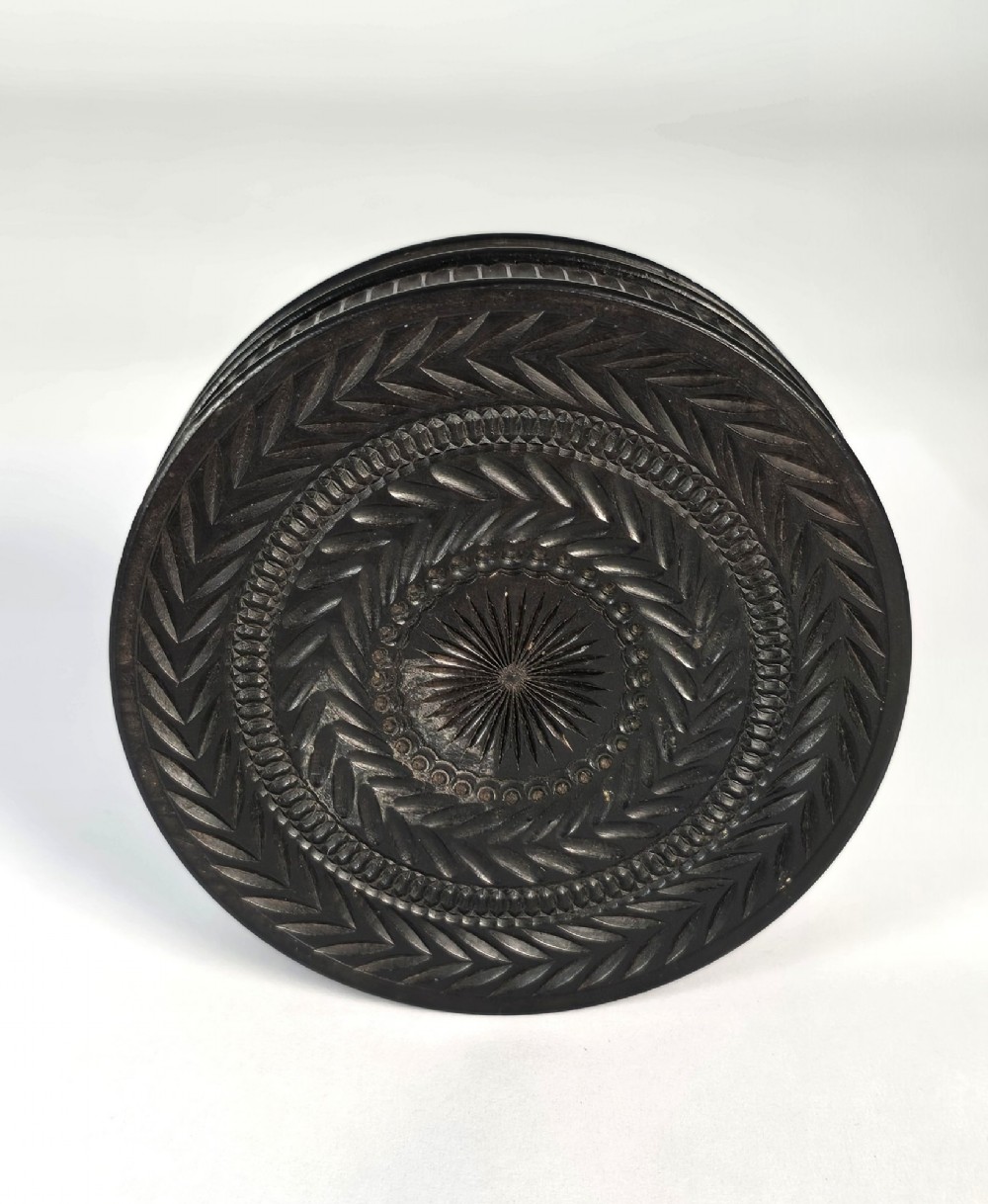 A circular black ebony snuff box with intricate engine-turned geometric patterns and raised beaded details on the lid. View V