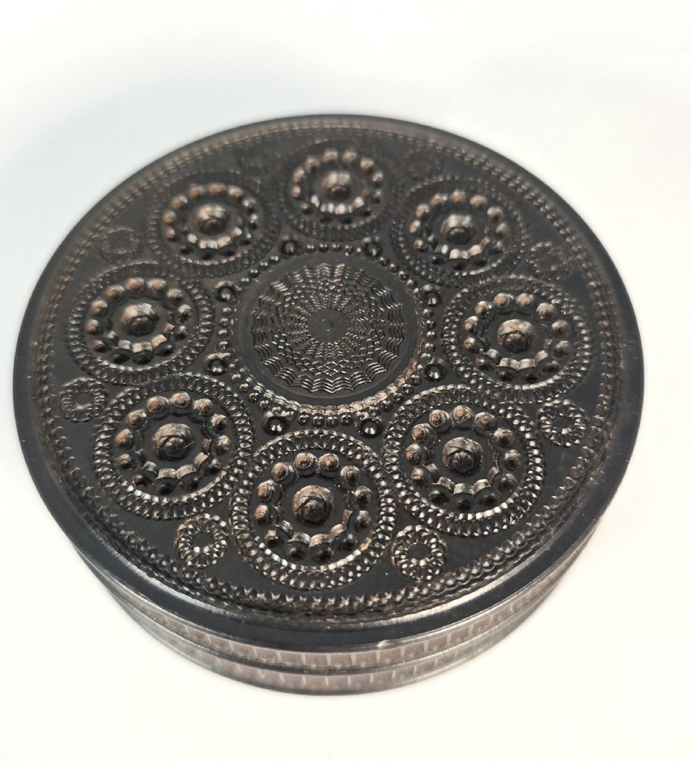 A circular black ebony snuff box with intricate engine-turned geometric patterns and raised beaded details on the lid. View VI