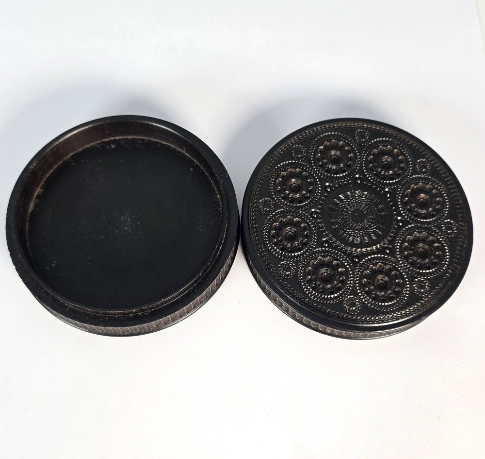 A circular black ebony snuff box with intricate engine-turned geometric patterns and raised beaded details on the lid. View VII