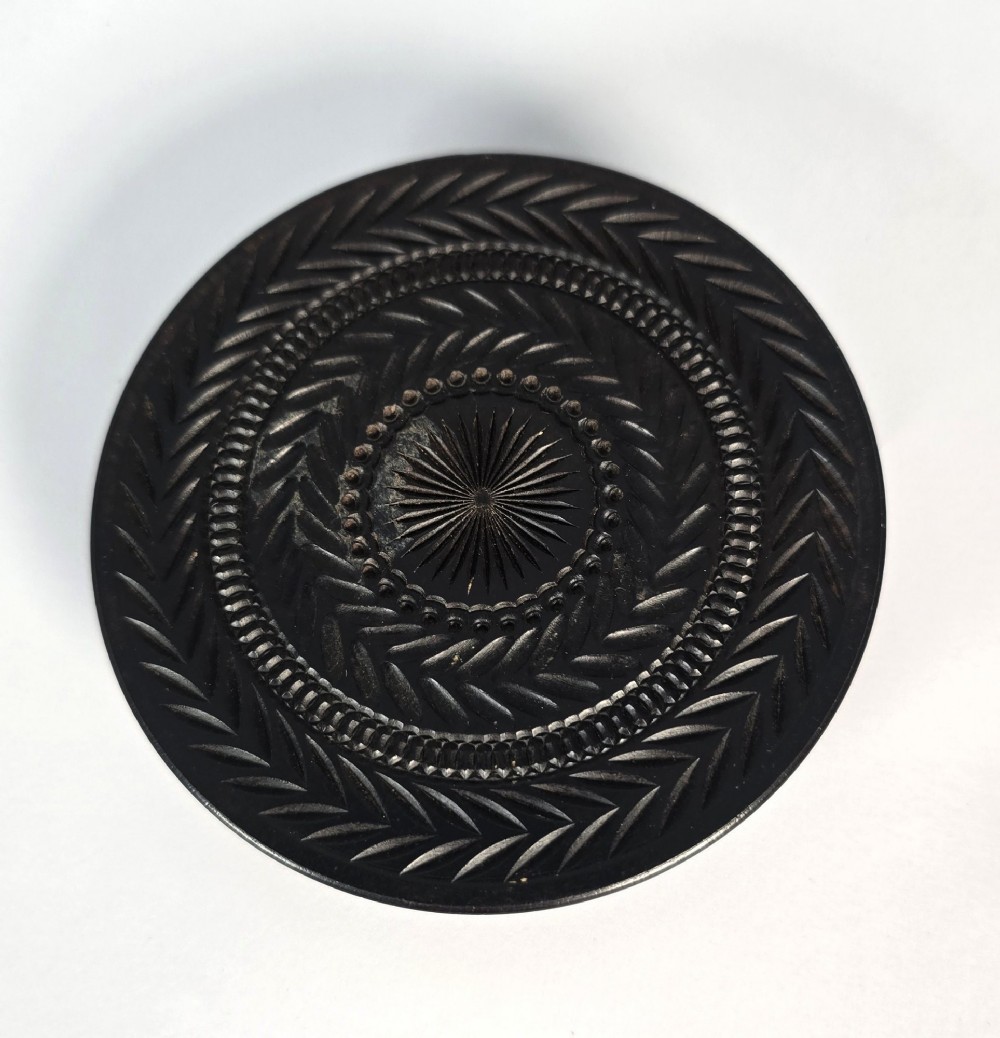 A circular black ebony snuff box with intricate engine-turned geometric patterns and raised beaded details on the lid. View IX