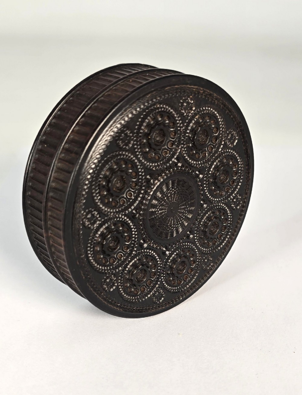 A circular black ebony snuff box with intricate engine-turned geometric patterns and raised beaded details on the lid. View XI