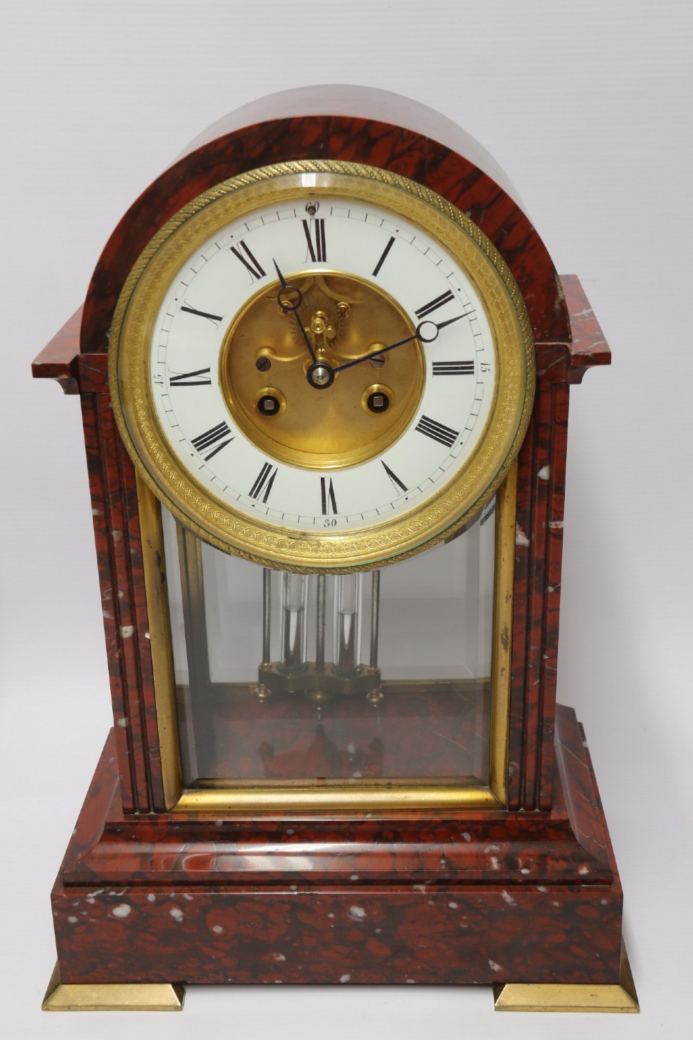 A late nineteenth-century French clock garniture in mottled red marble and gilt brass, featuring a central arch-topped mantel clock with a visible pendulum and two flanking urn cassolettes. View II