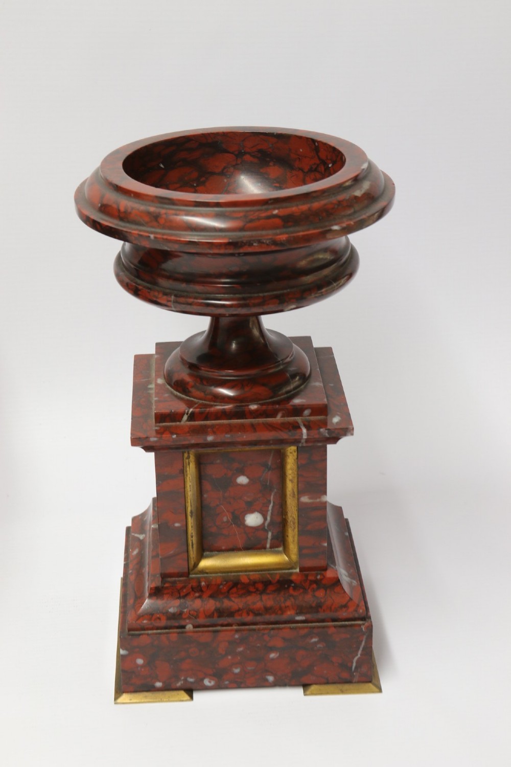 A late nineteenth-century French clock garniture in mottled red marble and gilt brass, featuring a central arch-topped mantel clock with a visible pendulum and two flanking urn cassolettes. View III