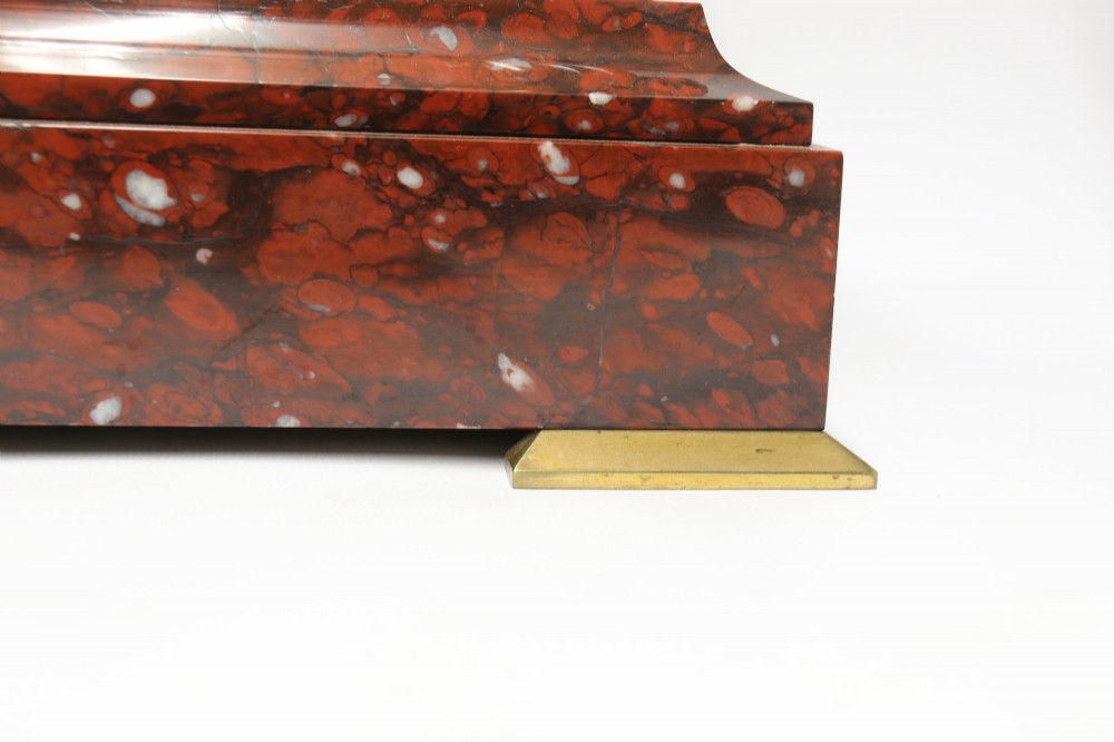 A late nineteenth-century French clock garniture in mottled red marble and gilt brass, featuring a central arch-topped mantel clock with a visible pendulum and two flanking urn cassolettes. View IV