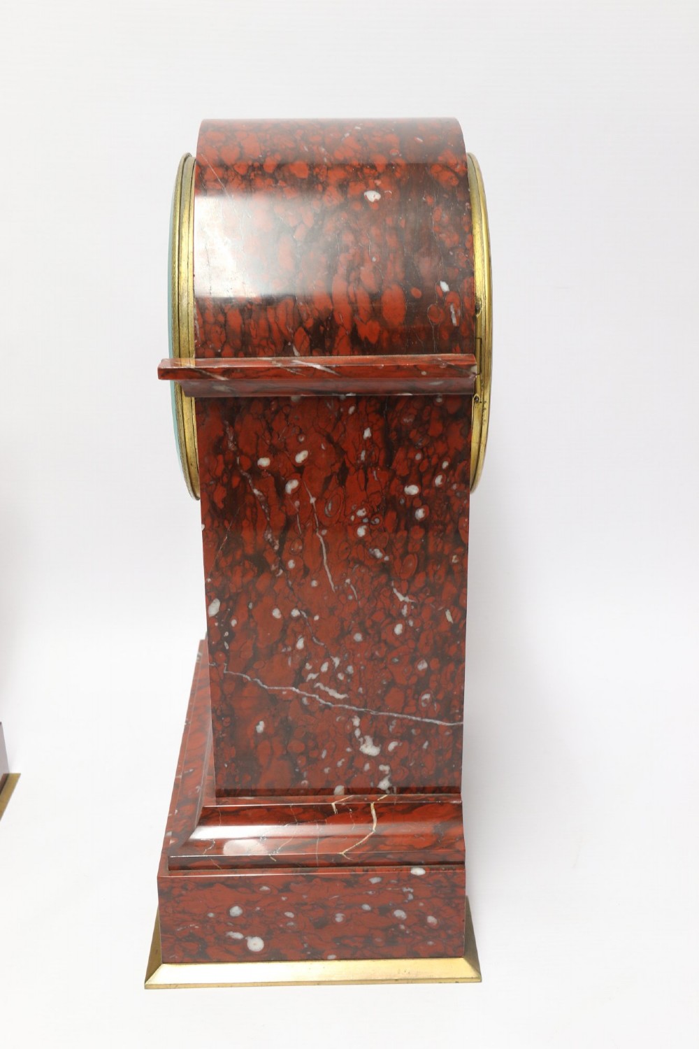 A late nineteenth-century French clock garniture in mottled red marble and gilt brass, featuring a central arch-topped mantel clock with a visible pendulum and two flanking urn cassolettes. View V