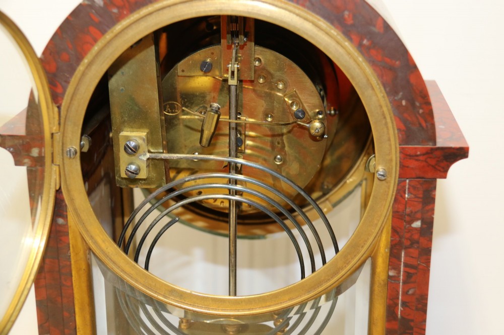 A late nineteenth-century French clock garniture in mottled red marble and gilt brass, featuring a central arch-topped mantel clock with a visible pendulum and two flanking urn cassolettes. View VI