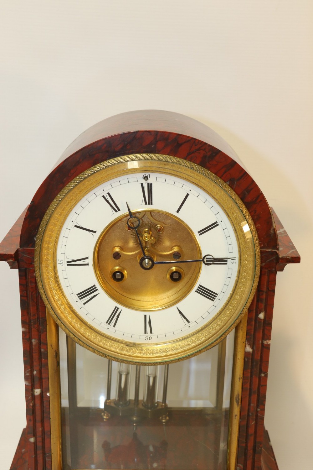 A late nineteenth-century French clock garniture in mottled red marble and gilt brass, featuring a central arch-topped mantel clock with a visible pendulum and two flanking urn cassolettes. View X