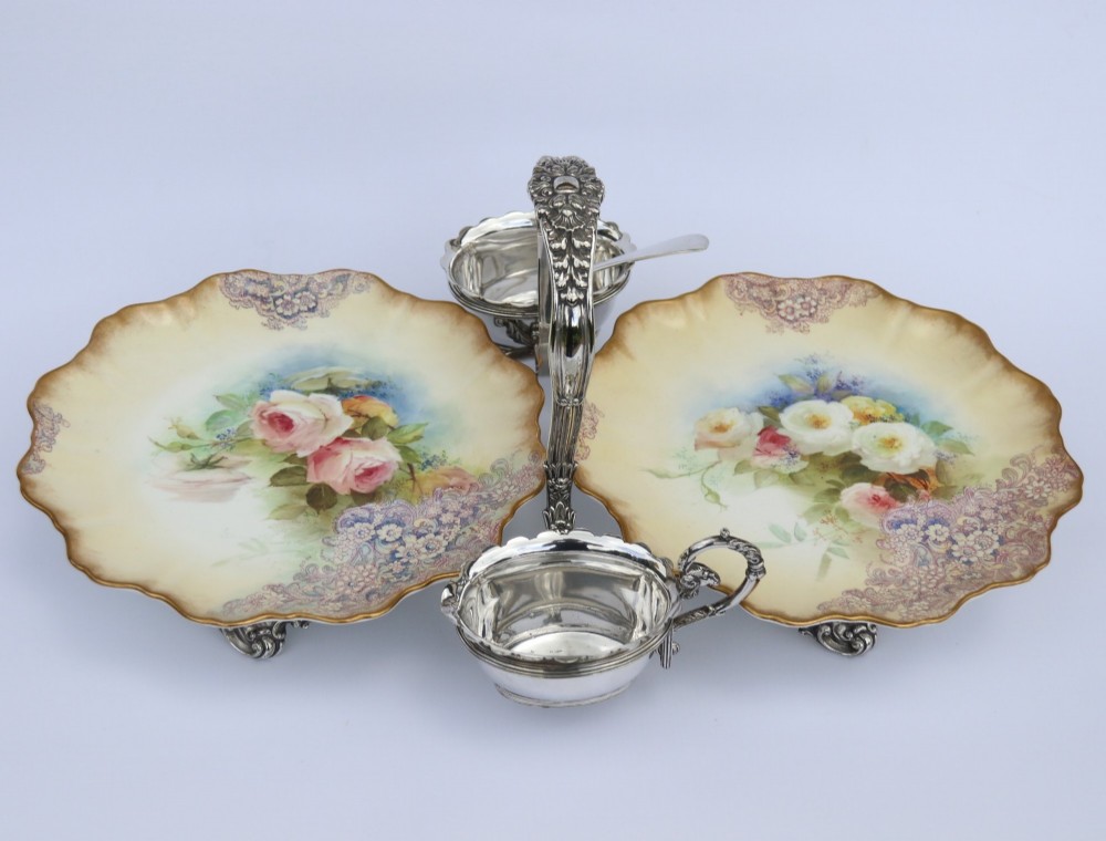 A silver-plated double frame holding two floral porcelain plates alongside a fitted cream jug and sugar bowl.