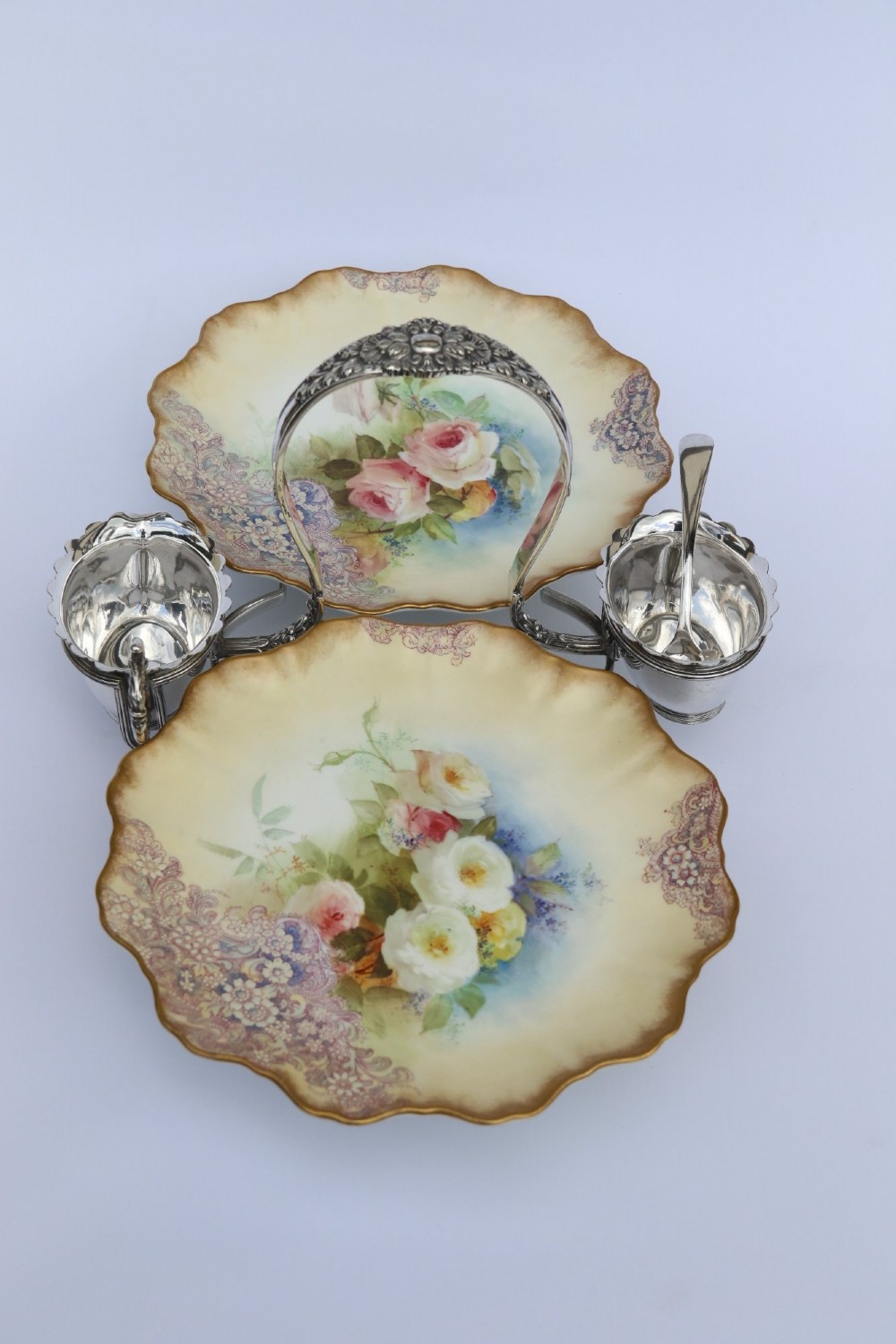 A silver-plated double frame holding two floral porcelain plates alongside a fitted cream jug and sugar bowl. View II