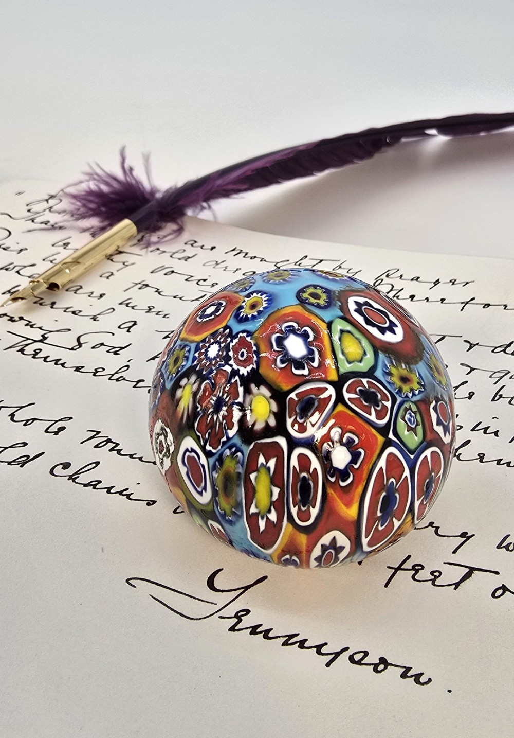 A spherical glass paperweight featuring a vibrant interior arrangement of colourful geometric and floral millefiori cane patterns.