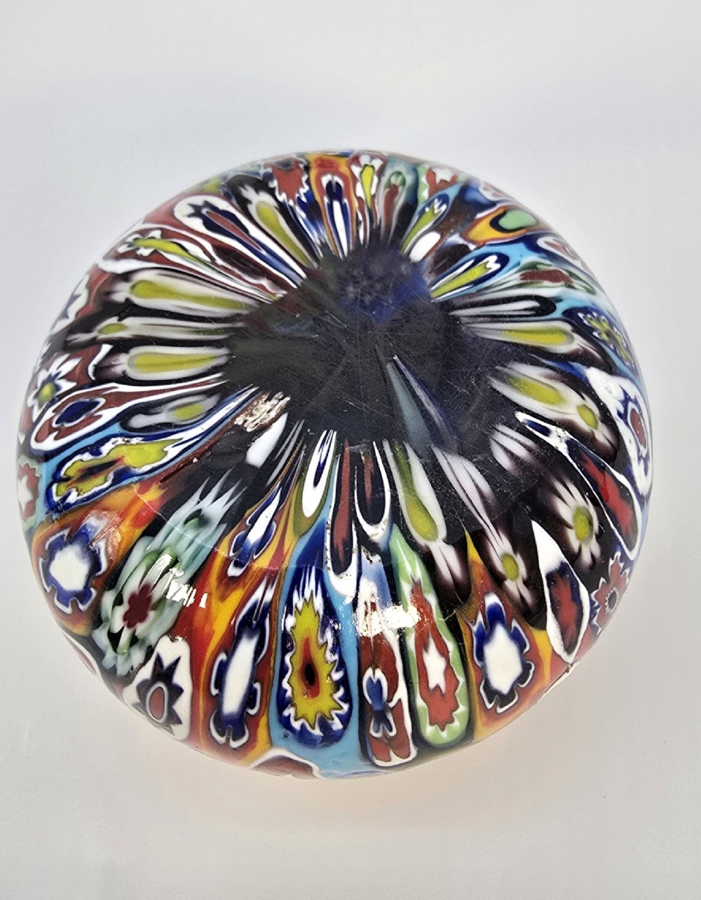 A spherical glass paperweight featuring a vibrant interior arrangement of colourful geometric and floral millefiori cane patterns. View III