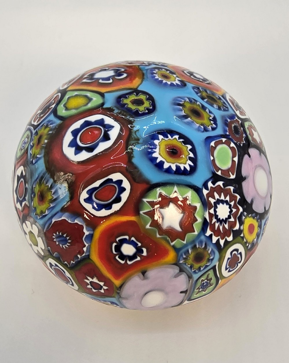 A spherical glass paperweight featuring a vibrant interior arrangement of colourful geometric and floral millefiori cane patterns. View IV