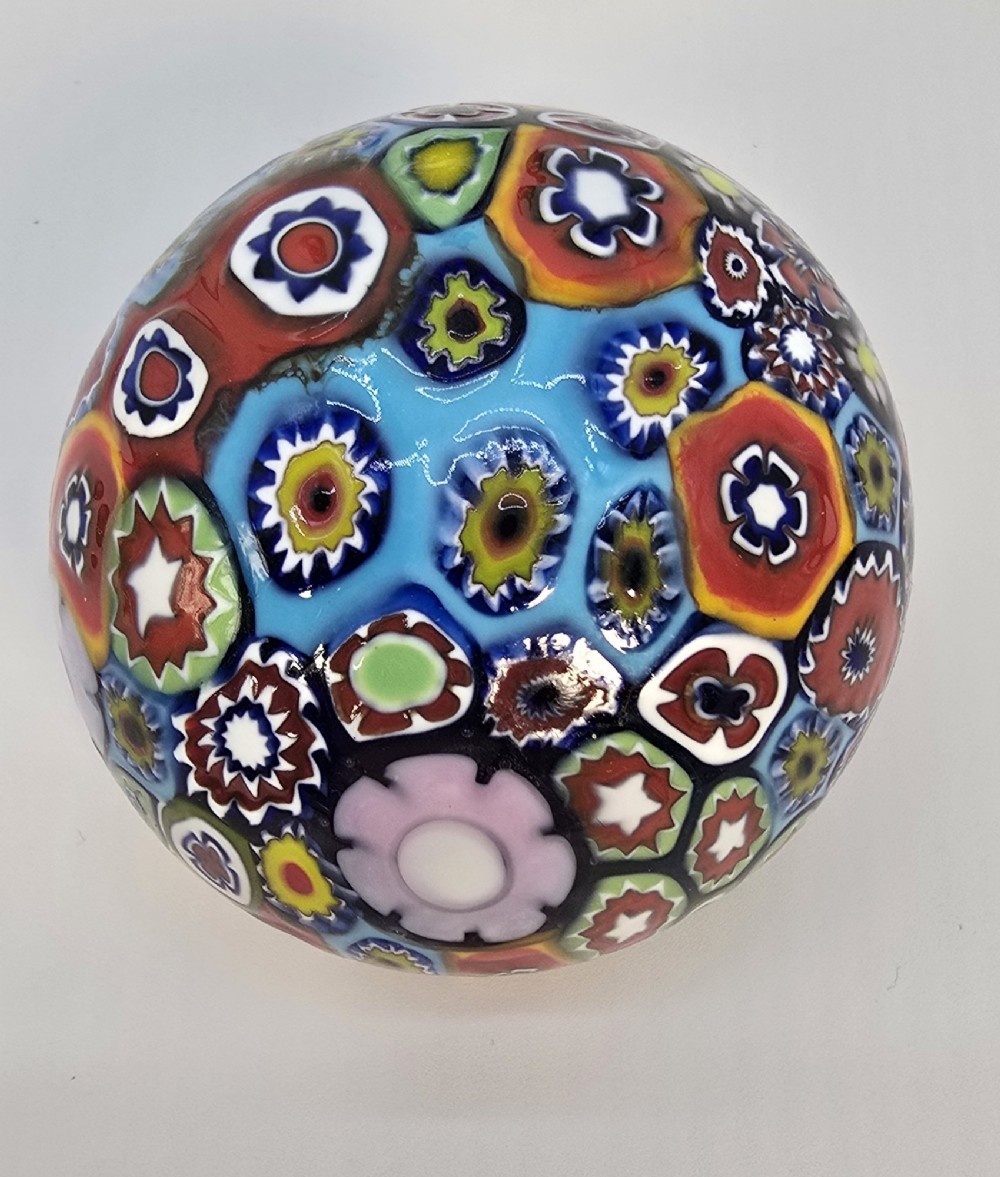 A spherical glass paperweight featuring a vibrant interior arrangement of colourful geometric and floral millefiori cane patterns. View V