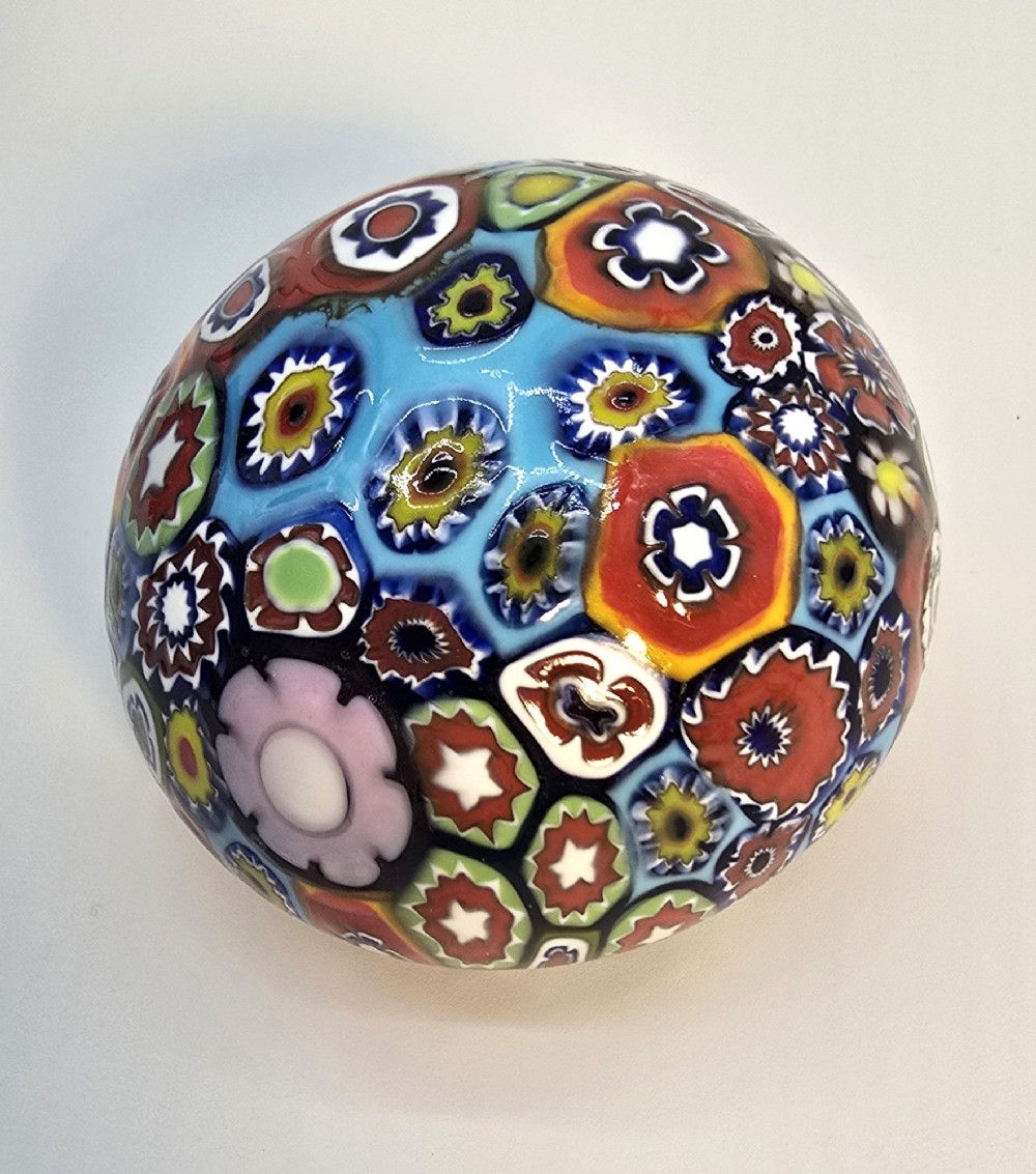 A spherical glass paperweight featuring a vibrant interior arrangement of colourful geometric and floral millefiori cane patterns. View VII