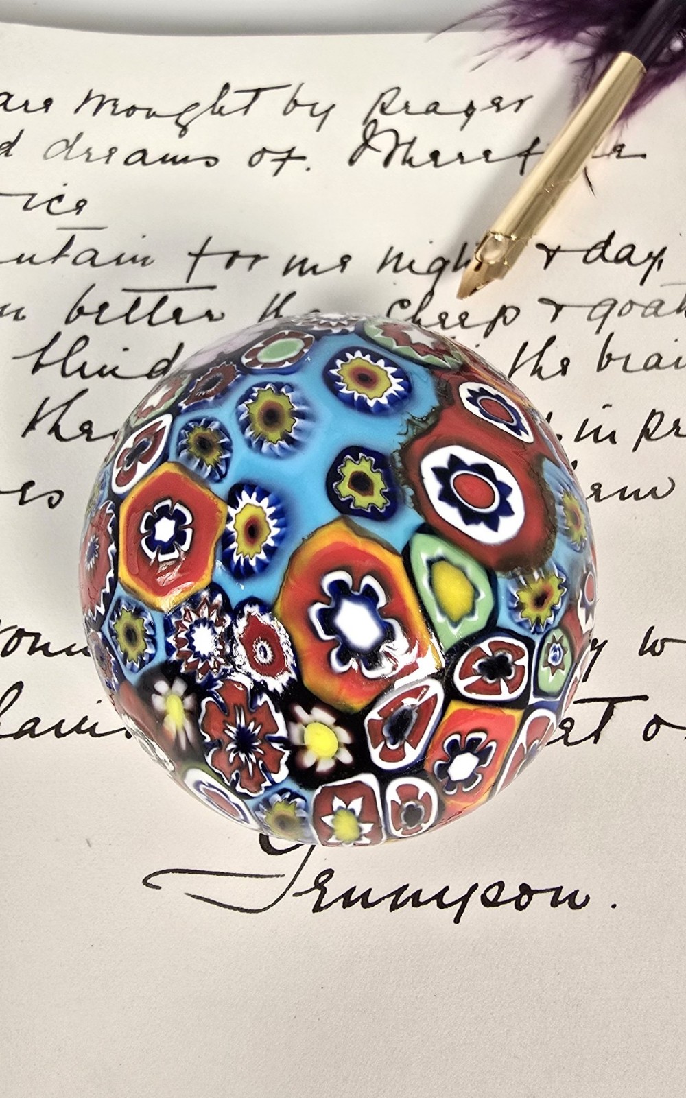 A spherical glass paperweight featuring a vibrant interior arrangement of colourful geometric and floral millefiori cane patterns. View X