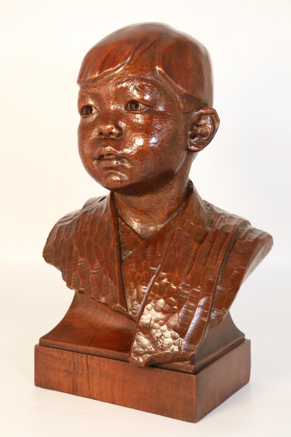 A carved walnut sculpture bust of a young child set upon a matching rectangular wooden plinth. View III