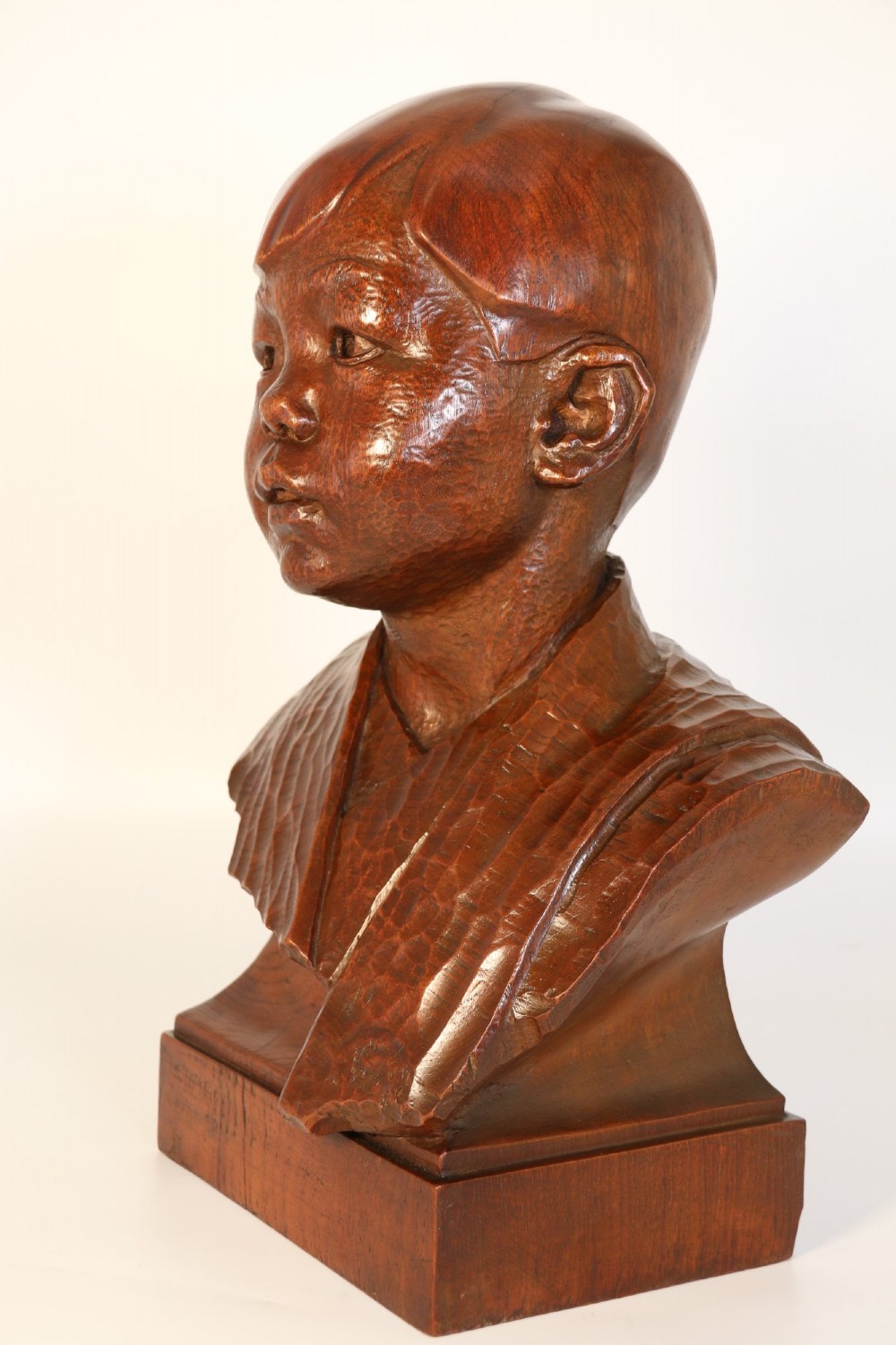 A carved walnut sculpture bust of a young child set upon a matching rectangular wooden plinth. View IV