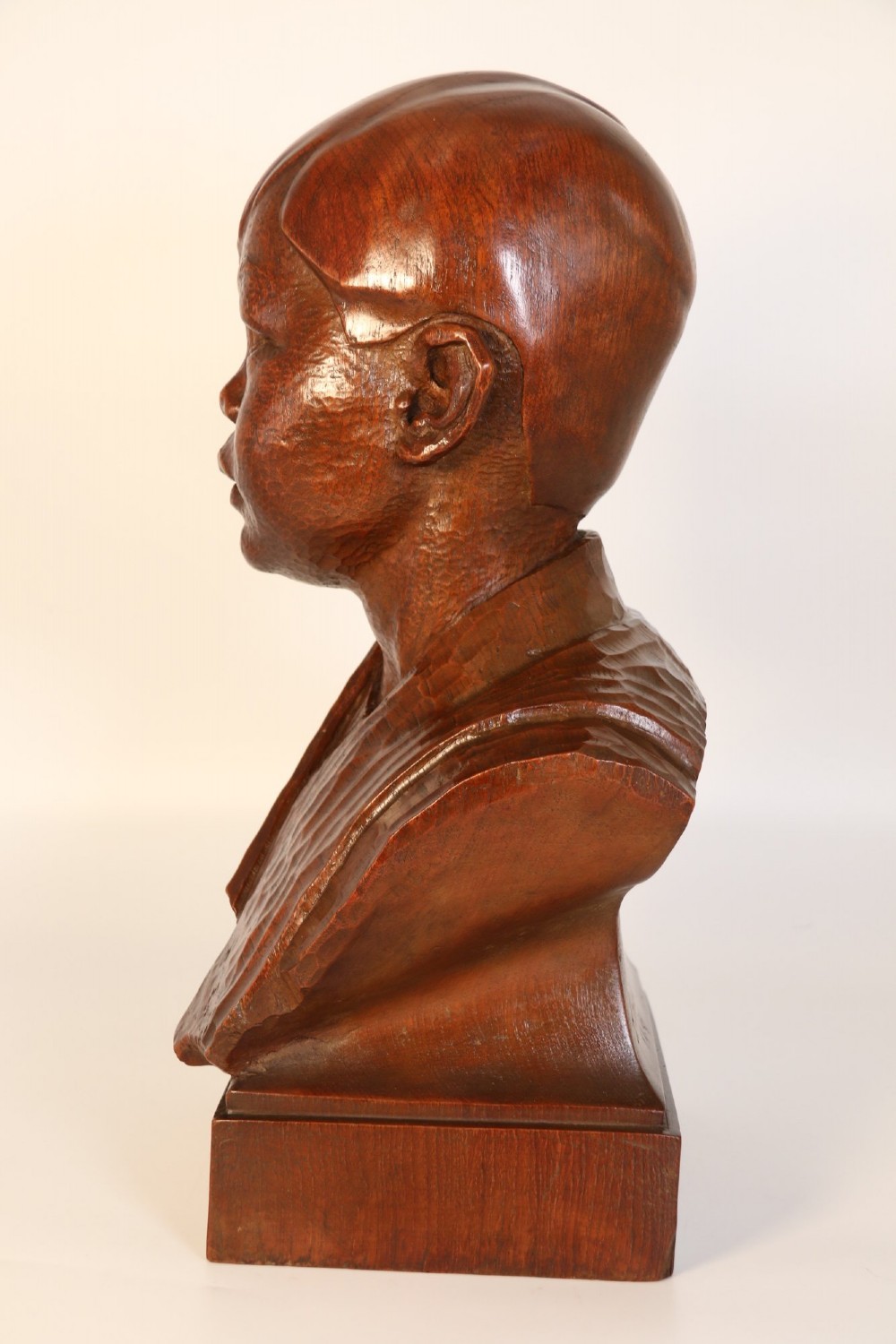 A carved walnut sculpture bust of a young child set upon a matching rectangular wooden plinth. View V
